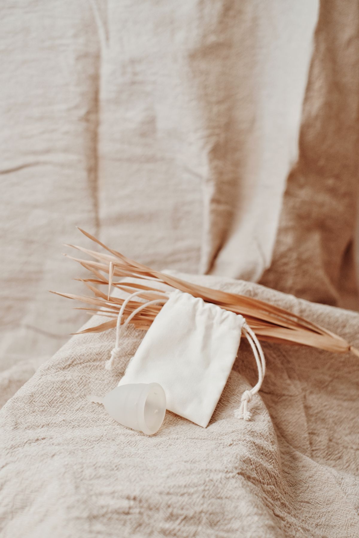 A generic translucent menstrual cup beside a white pouch on beige fabric.